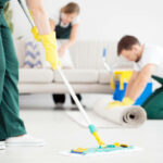 Cleaner in green overalls cleaning floor using mop in the flat interior